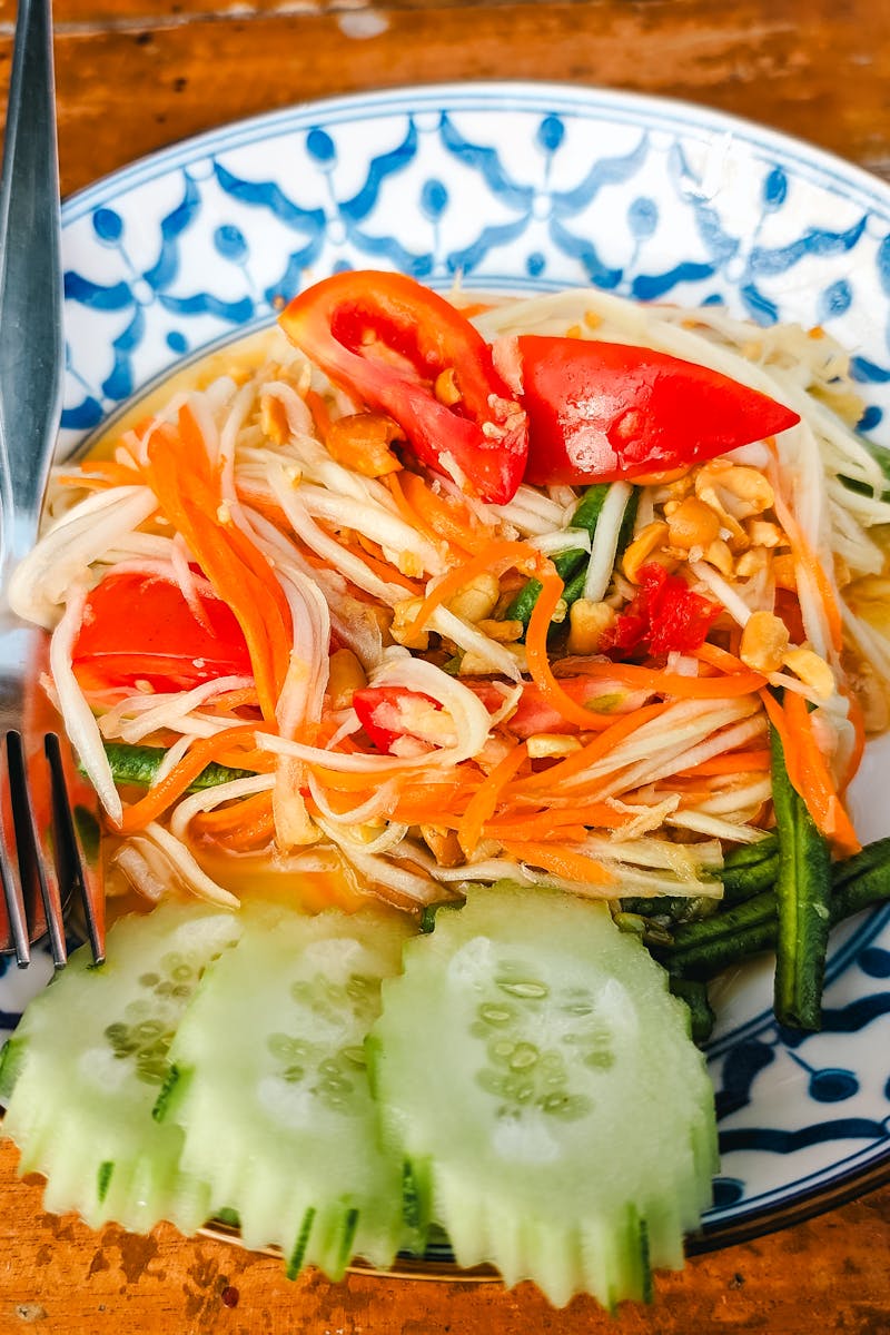 Vibrant close-up of Thai papaya salad with fresh vegetables on a traditional plate.