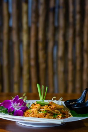 Close-up of a colorful Thai Pad Thai dish garnished with an orchid, captured indoors.